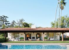 an outdoor swimming pool next to a white house with palm trees in the back ground