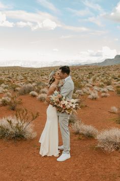 a bride and groom standing in the desert with their arms around each other as they kiss