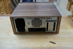 a small wooden computer case sitting on top of a hard wood table next to a screwdriver