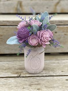 a pink mason jar with purple flowers and greenery in it sitting on a wooden bench