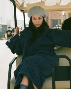 a woman in a blue coat and hat sitting on a golf cart with her legs crossed