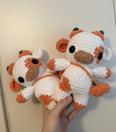 two crocheted stuffed animals are being held up by someone's hand in front of a white wall