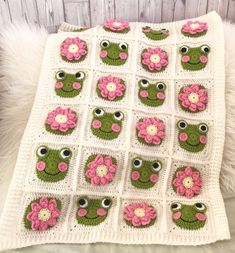 a crocheted blanket with pink flowers and green frog faces on it's sides