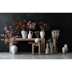 several vases and plants on a table in front of a dark wall with black walls