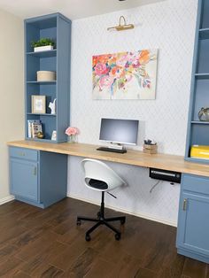 a desk with a computer on top of it in front of a blue bookcase