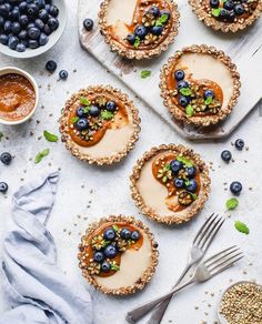 small pies with blueberries and other toppings on a white surface next to silverware