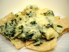 some tortilla chips with cheese and spinach on them sitting on a white plate