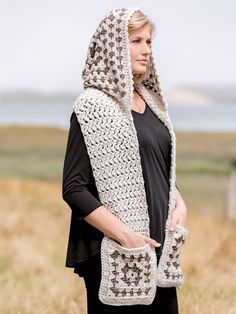 a woman standing in a field wearing a crochet hooded jacket and scarf with hood