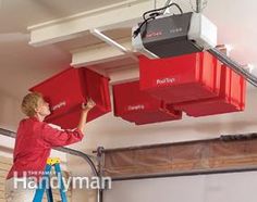 two men working on some red boxes in a garage, one is hanging from the ceiling