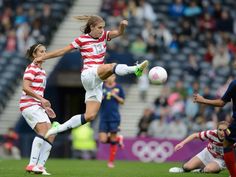 two women are playing soccer in front of an audience at a sporting event, one is about to kick the ball