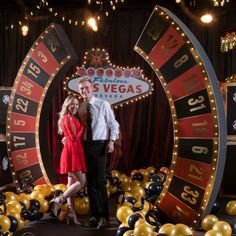 a man and woman standing in front of a wheel of fortune sign at the las vegas strip