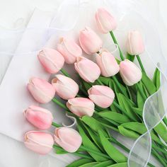 a bouquet of pink tulips sitting on top of a white sheet with ribbon