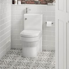 a white toilet sitting in a bathroom next to a brick wall and tiled flooring