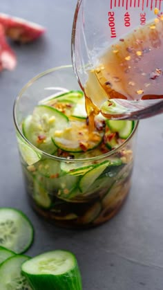 a person pouring dressing into a glass bowl filled with cucumbers and other vegetables