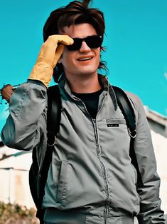 a man with sunglasses and a backpack is holding his hand up to his face as he stands in front of a blue sky