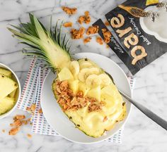 a pineapple topped with bananas and nuts next to a bowl of yogurt