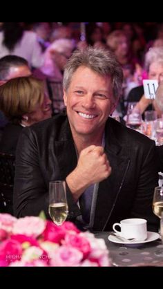 a man sitting at a table with two wine glasses in front of him and smiling