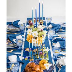 a table set with blue and white plates, silverware, candles and flowers on it