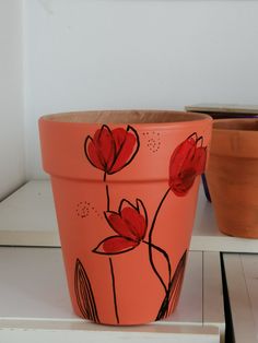 an orange flower pot sitting on top of a white shelf next to two pots with red flowers painted on them