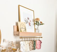 there is a vase with flowers on the shelf next to some clothes hanging from hooks