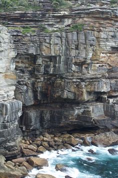 an image of a rocky cliff by the ocean with waves coming in from the rocks