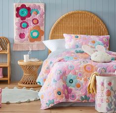 a bedroom with blue walls and pink flowers on the bedspread, two baskets for storage and a wicker headboard