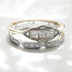 two wedding rings with diamonds on them sitting on a white tableclothed surface in front of the camera