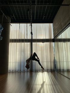 a person doing a handstand on a suspended object in an empty room with curtains