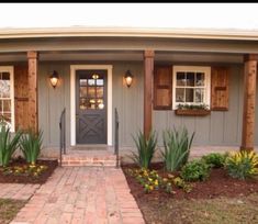 a gray house with wooden shutters and brick walkway leading to the front door area