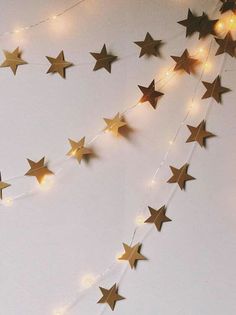 a string of gold stars hanging from the ceiling next to a white wall with lights on it