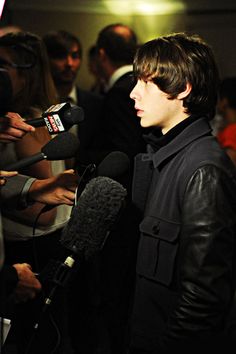 a man standing in front of microphones surrounded by reporters