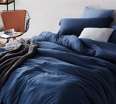 a bed with blue comforters and pillows in a white room next to a chair