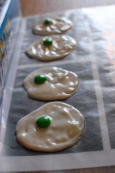 four cookies with white icing and green candies on the top are lined up in a row