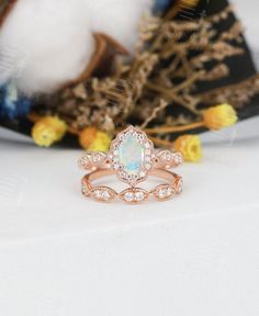 an opal and diamond ring sitting on top of a white table next to flowers