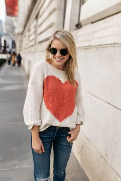 a blonde woman wearing jeans and a heart sweater