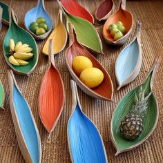 several leaf shaped bowls filled with fruit on top of a woven tablecloth covered floor