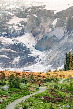 a person walking down a trail in the mountains with snow on the mountain behind them