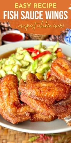 fish sauce wings served with cucumbers and tomatoes on a white plate over a woven place mat