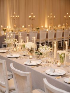 a long table with white flowers and candles is set for a formal dinner or reception