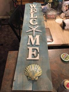 a wooden sign that says welcome home with a seashell on the front and bottom