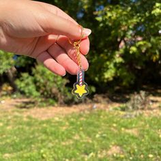 a hand holding a small yellow star shaped keychain in front of some trees