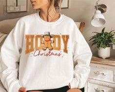 a woman sitting on top of a bed wearing a white christmas sweater with a teddy bear