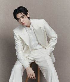 a young man in a white suit sitting on a chair with his hands on his hips