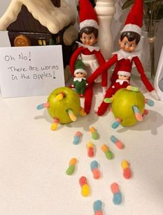 two elfs sitting on top of an apple next to candy candies and a sign that says, oh no there are worms in the apples