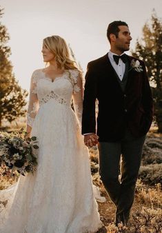 a bride and groom holding hands walking through the grass in front of some pine trees