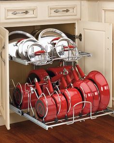 the rack is full of red pots and pans in this kitchen cabinet with white cabinets