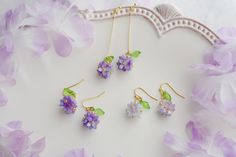 purple flowers and green leaves are hanging from gold earwires on a white background