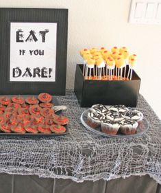 a table topped with cupcakes and cake next to a sign that says eat if you dare