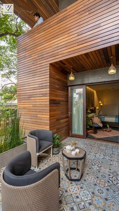 an outdoor living area with two chairs and a coffee table on the ground next to a wooden wall