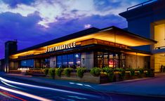 the outside of a restaurant at night with lights streaking down on it's side